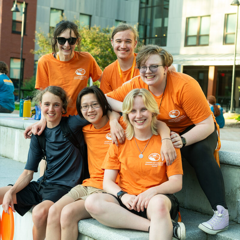 Group of friends smiling sitting in front of Champlain College academic building