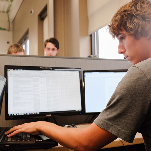 Student working on a computer with multiple screens